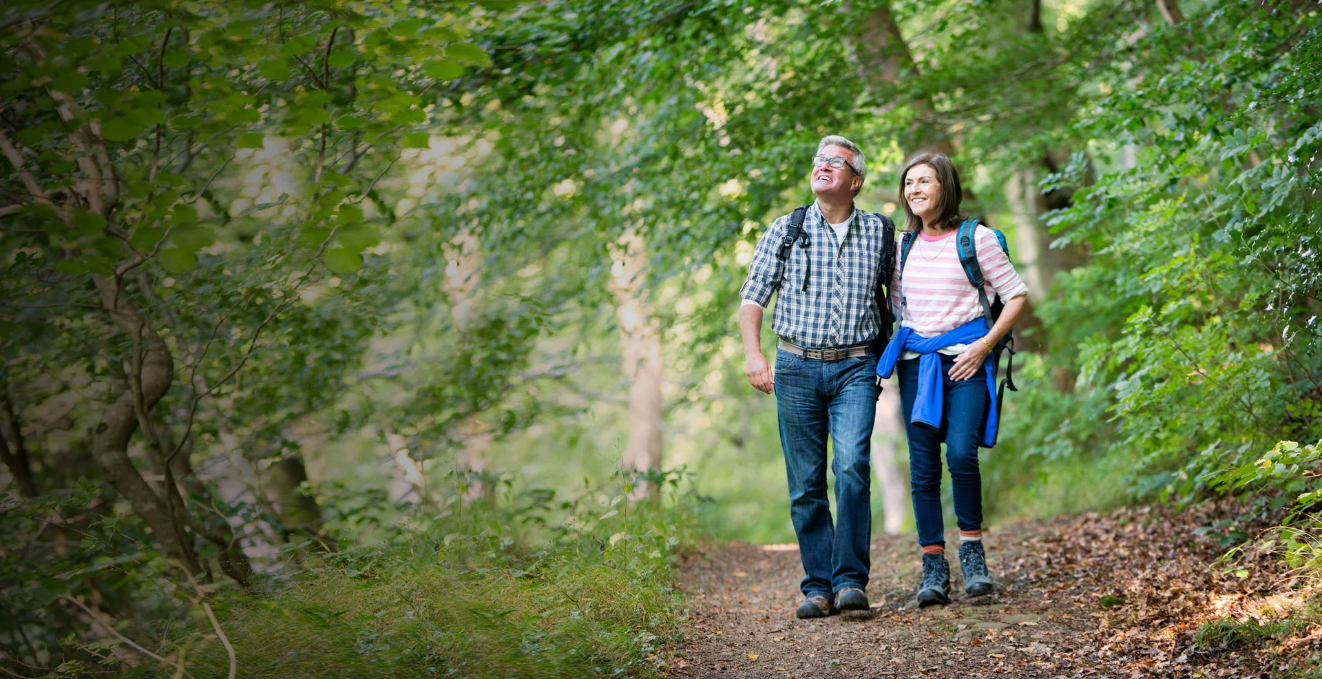a man and woman walking on a trail in the woods